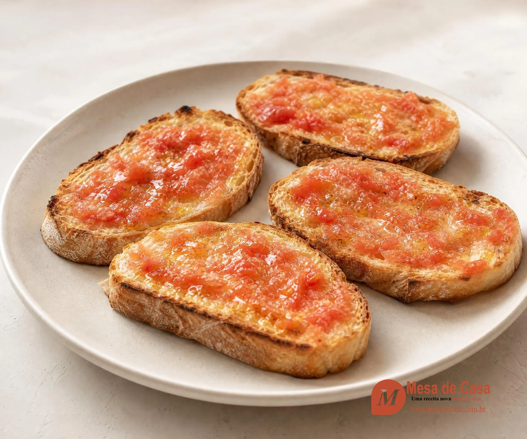 Quatro fatias de pão tostado cobertas com tomate ralado e azeite em prato claro